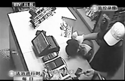 戴帽男子一手掐住加油站營(yíng)業(yè)員，一手持發(fā)令槍指向另一營(yíng)業(yè)員，要求“把錢給我裝起來”。