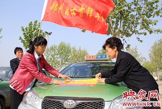 　　授旗結(jié)束后，首都的士雷鋒車隊王鳳進隊長（右）與鄭州的的哥的姐在車身上貼上標識。