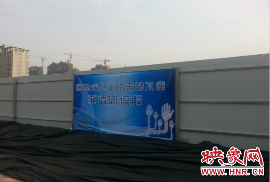 道路南側(cè)圍起了白色的圍擋，墻上標(biāo)示著“因地鐵施工帶來(lái)的不便敬請(qǐng)您諒解”的提示牌。