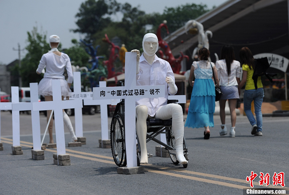 4月16日，重慶市洋人街上擺放著兩個(gè)受了傷的塑料人像“模特”，旁邊十字架上寫(xiě)著向“中國(guó)式過(guò)馬路”說(shuō)不