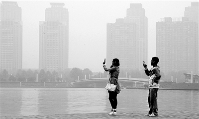 29日中午，鄭東新區(qū)如意湖畔，兩個年輕人拍攝霧霾中的景色。 鄭州晚報記者 馬健 圖