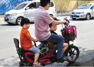 周先生騎著一輛低矮的電動車帶著一對兒女，很不安全。