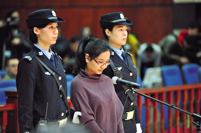 被告人盧梅低著頭，站在朝陽法院刑事審判庭的被告席上。